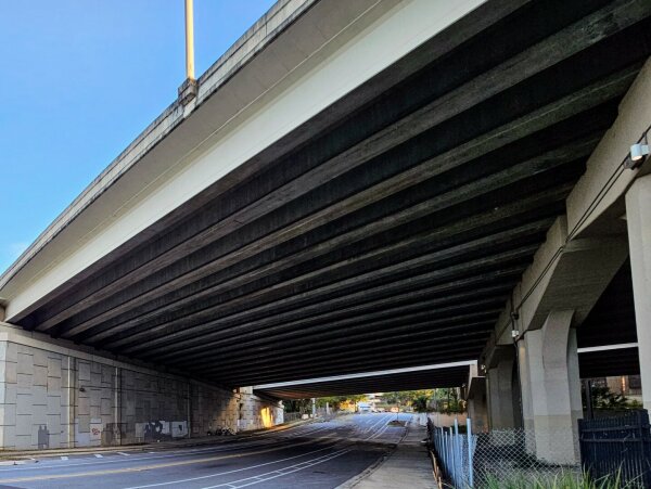 Tunnel like underpass in an undeserved neighborhood, with barbed-wire on one side, preventing access underneath, and remnants of a tent-home on the other end.