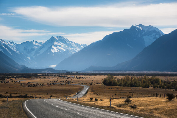 a landscape with the winding road in the foreground going into distance and the hazy mountains in the background during daytime in New Zealand